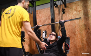 Voluntario asistiendo a un atleta en silla de ruedas en un entrenamiento ordinario adaptado